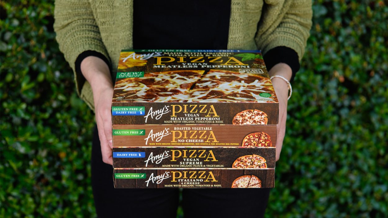 A person holding a stack of Amy's pizza packages